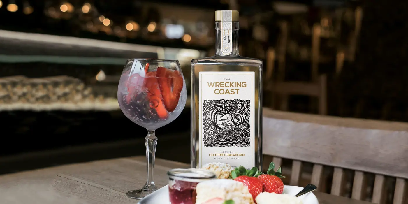 Cornish Clotted Cream Gin Spirit Label Design 2560x1280 A Cornish Clotted Cream Gin bottle next to a glass of gin with strawberries and plated ingredients of a traditional Cornish cream tea