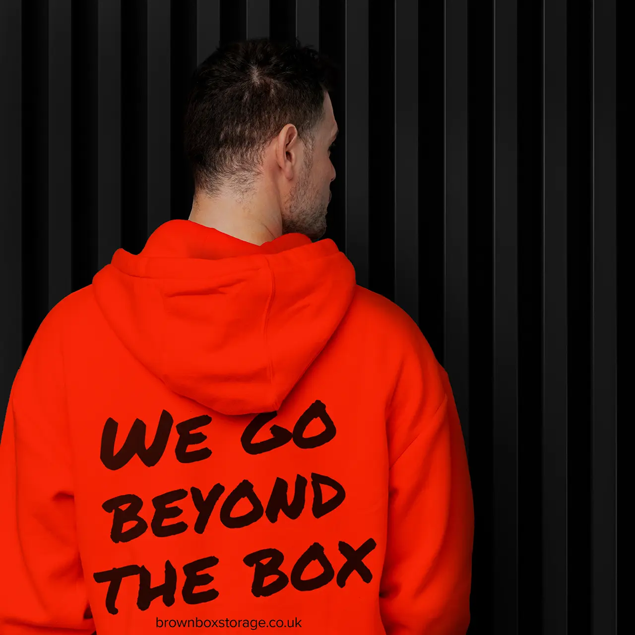 A gentleman with his back to the camera wearing a Brown Box Self Storage Branded hoodie in orange with black text on it.