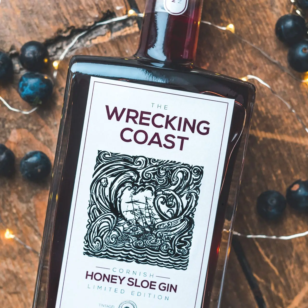 Cornish Honey Sloe Gin 1280x1280 A photograph of Thew Wrecking Coast Distillery Honey Sloe Gin bottle on wooden table top surrounded by sloes