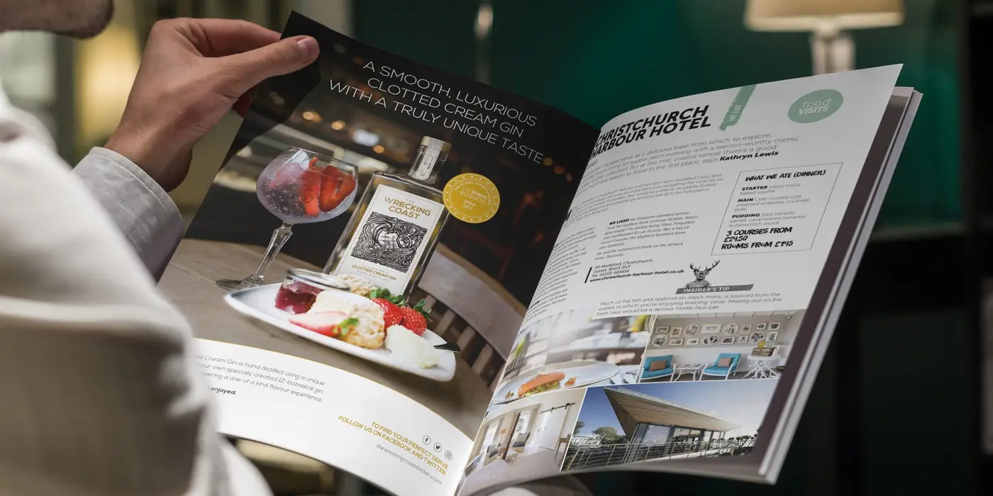 The Wrecking Coast Distillery Brand Brochure Design 2560x1280 A seated man reading a magazine whilst looking at a Wrecking Coast Distillery advert in a food and spirit magazine