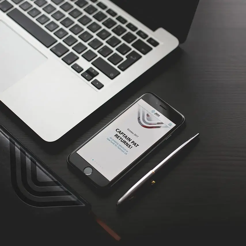 The screen of a phone showing the website news page design for mobile as it sits next to a laptop pen and branded folder.